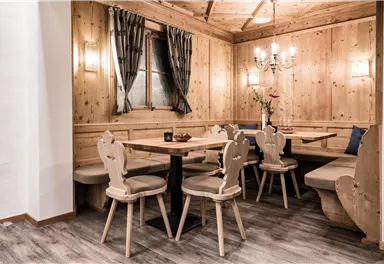 A cozy dining room with wooden walls and a modern table. There are several chairs and a bench, surrounded by stylish curtains.
