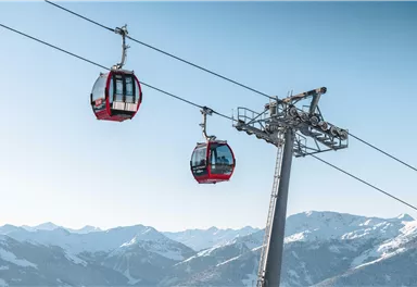 Eine Aussichtsbahn fährt über schneebedeckte Berge. Der klare Himmel und die Berglandschaft schaffen eine beeindruckende Kulisse.