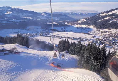 Eine wunderschöne Winterlandschaft mit verschneiten Bergen und einem Skilift. Im Hintergrund ist ein ruhiges Dorf zu sehen.