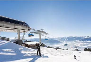Eine Skiliftanlage vor einer schneebedeckten Landschaft. Ski- und Snowboardfahrer genießen den klaren blauen Himmel.