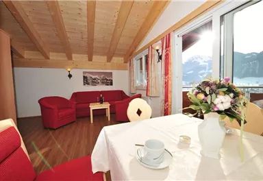 A cozy living room with a red sofa and table. Large windows offer a view of the mountains and plenty of daylight.