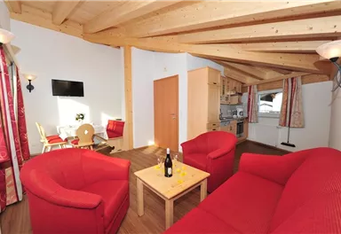 A bright apartment with wooden ceilings and a red sofa. The room features a kitchenette and a dining area.