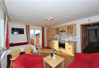 A cozy holiday apartment with a modern kitchen and a living area. Red armchairs and a dining table create an inviting atmosphere.