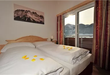A cozy bedroom with two beds and decorative flower petals. The impressive mountains are visible through the window.