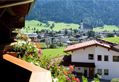 A picturesque landscape with traditional houses and blooming flowers. In the background, gentle hills and a church are visible.
