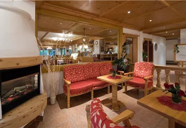 A cozy seating area with red upholstered sofas and a fireplace. The room has warm wooden paneling and an inviting atmosphere.