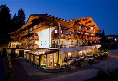 A charming hotel with balconies adorned with flowers. The lights glow warmly in the twilight.