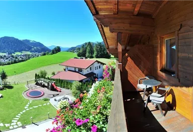 A picturesque view from a balcony overlooking a green landscape with mountains in the background. The garden is beautifully landscaped and features a pond as well as cozy seating areas.