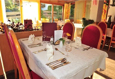 A beautifully set table in a restaurant with a red chair and an elegant tablecloth. A versatile arrangement of cutlery and glasses creates an inviting atmosphere.