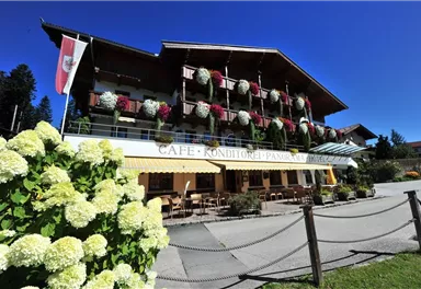 A charming café with a balcony adorned with flowers. The facade is designed in a traditional style and surrounded by a beautiful garden.