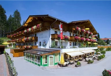 A cozy café with blooming balcony plants and sunny terraces. It is located in a picturesque setting with lots of greenery.