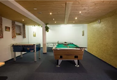 A game room with a pool table and a foosball table. The walls are brightly painted and there is cozy lighting.