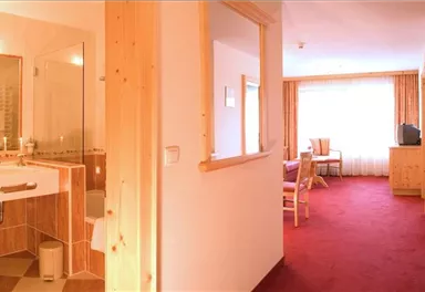 A cozy room with a bathroom and a small kitchenette. The room has a warm carpet and large windows for plenty of natural light.