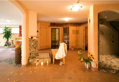 A relaxing wellness area with wooden paneling and gentle light sources. The room features plants, candles, and access to the sauna.