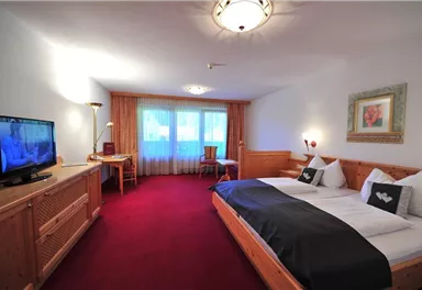A cozy hotel room with a large double bed and a television. The room is bright and friendly, with a table and chairs as well as a beautiful view through the window.