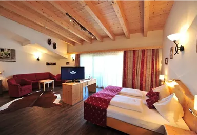 A cozy hotel room with a wooden ceiling and modern furniture. The room has a double bed, a seating area, and a television.