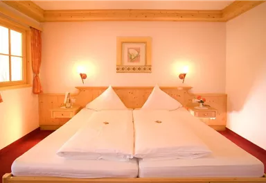 A cozy bedroom with a large double bed and wooden decor. The room is well-lit and has a window with a view.