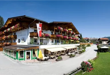 A cozy hotel in alpine style with balconies adorned with flower boxes. Surrounded by a picturesque landscape and lots of greenery.
