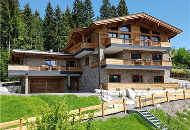 A modern house made of wood and stone, surrounded by green trees and lawn. The clear sky and the tranquil surroundings create an inviting atmosphere.