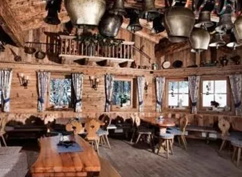 A cozy, wood-paneled room with rustic tables and chairs. Various bells are hanging from the ceiling, and the winter landscape is visible through the windows.