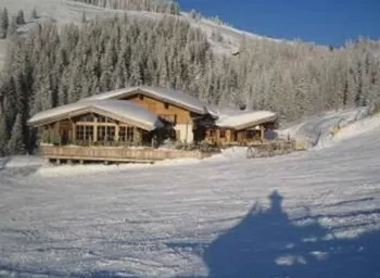 A cozy chalet in a snowy winter landscape. Surrounded by snow-covered trees and clear blue sky.