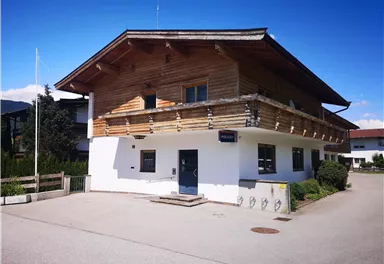 Ein modernes Gebäude mit einer Holzfassade und einem Balkon. Es steht in einer ruhigen Umgebung mit einem klaren blauen Himmel.
