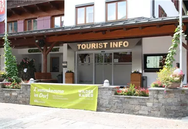 Ein Gebäude mit dem Schild "TOURIST INFO" an der Fassade. Vor dem Eingang stehen Blumen und Pflanzen in Töpfen.