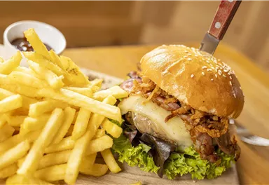 Ein saftiger Burger mit knusprigem Belag und frischem Gemüse. Dazu gibt es goldbraune Pommes frites.