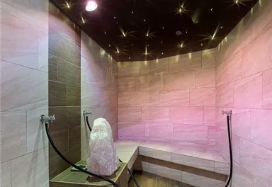 A modern steam bath area with gentle lighting effects. The walls are elegantly tiled, and there are benches made of wood.