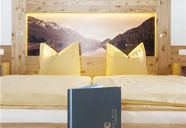 A cozy hotel room with a large bed and yellow pillows. There is also a black book on the wooden floor.