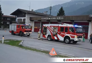 Zwei Feuerwehrfahrzeuge stehen vor der Feuerwehrstation in Söll. Im Hintergrund sind Berge und eine ländliche Umgebung zu sehen.