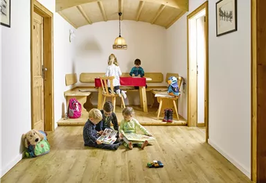 Ein heller Raum mit Holzfußboden, in dem vier Kinder spielen. Am Tisch sitzt ein weiteres Kind und malt.