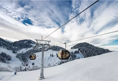 A cable car rides over snow-covered mountains. The sky is partly cloudy and the landscape is wintery beautiful.