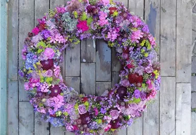 Ein wunderschöner Blumenkranz in verschiedenen Lila- und Grüntönen. Er ist reich verziert mit Rosen und anderen bunten Blumen.
