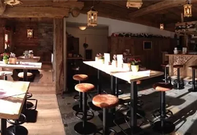 Ein gemütliches Restaurant mit rustikaler Einrichtung und Holztischen. Die Atmosphäre ist warm und einladend, mit viel Licht von den Fenstern.