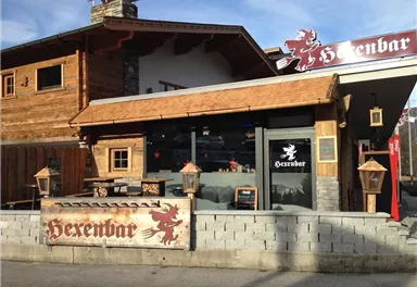Ein rustikales Gebäude mit einem Holzdesign, das als Hexenbar bekannt ist. Die Fassade zeigt ein Schild und einige dekorative Laternen.