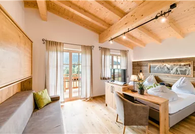 A modern room with wooden furniture and large windows. There is a bed, a seating area, and a desk.