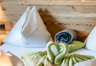 A cozy hotel room with a double bed and artfully folded towels in the shape of swans. In the background, there is a picture of horses.
