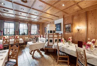 A cozy restaurant with wooden decor and elegantly set tables. The windows are adorned with curtains, creating an inviting atmosphere.