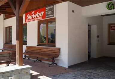 A protected entrance area with two benches and large windows. A sign with the inscription "SkiWelt" hangs on the wall.