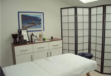 A quiet room with a treatment table and a room divider. On the wall hangs a picture and some utensils that promote relaxation.