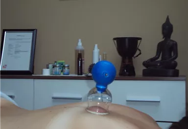 A therapeutic treatment using a cupping method on a person's back. In the background, various products and a Buddha statue can be seen.