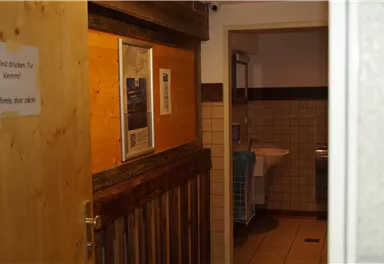 A view into a hallway with wooden paneling and a washroom. The room is brightly lit and well-maintained.
