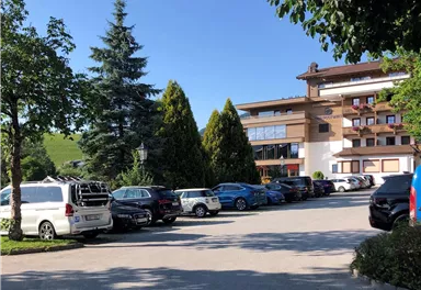 A parking lot in front of a building with several cars and trees. The sky is clear and blue.