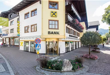A modern bank building at a street corner. Flower beds and a clear view of the sky complete the scene.