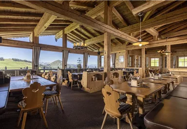 Ein gemütliches Restaurant mit Holzmöbeln und großen Fenstern. Der Blick auf die grüne Landschaft sorgt für eine einladende Atmosphäre.