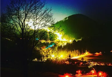 Eine nächtliche Landschaft mit leuchtenden Lichtern und einem sanften Hügel im Hintergrund. Der Himmel hat einen klaren Verlauf von Dunkelblau zu einem sanften Licht.