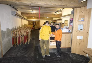 Eine gemütliche Berghütte mit Holzdekor und einem Empfangsbereich. Zwei Personen stehen lächelnd im Vordergrund, bereit für ein Abenteuer in der Natur.