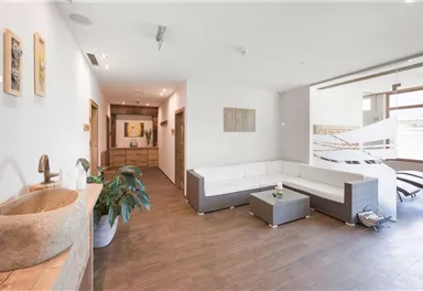 A modern living room with a bright decor and a large sofa. The room has large windows and plenty of daylight.
