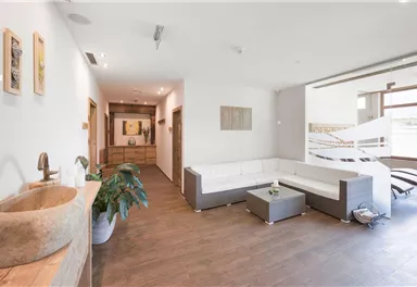 A modern living room with a bright seating area and wooden floor. In front of the window, there are lounge chairs and there are subtle decorative elements.